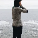 A woman standing by the ocean with hand on head.