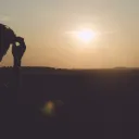 A young man sitting with head resting on tips of his finger. The sun is setting in the background.