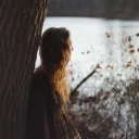 A young woman leaning up against a tree.