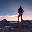 A person standing on top of a rocky hill watching the sunset.