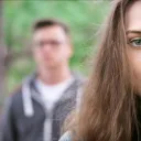 A young couple - woman in the foreground, man in the background blurred.