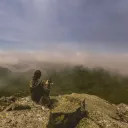A woman sitting on cliff edge with her dog.