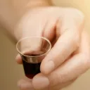 A man holding a small clear cup of wine.