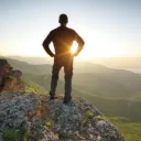 A young man standing at the edge of cliff looking at the setting sun.
