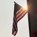 A photo of the American flag with the sun rising behind it.