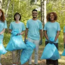 five people wearing matching blue shirts and holding garbage bags while standing outside