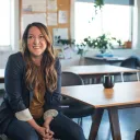 a smiling woman sitting in a chair next to a wooden table
