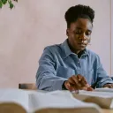 a woman sitting at a table and looking at two open Bibles