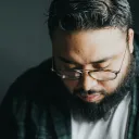 A man with a beard and wearing glasses has his head bowed.
