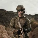a soldier holding a weapon with a brown hilly terrain in the background