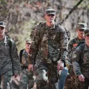 a group of young men wearing army camouflage uniforms and walking outdoors