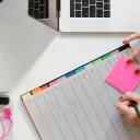 a pair of hands writing in a planner and holding a pink notepad