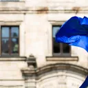 A European Flag blowing in the wind outside of an old building.
