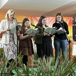 four ladies singing on a stage with plants in the foreground
