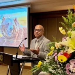 2024 Feast of Tabernacles Penang, Malaysia a man standing at a lectern with a floral arrangement on one side and a projector screen on the other