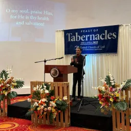 2024 Feast of Tabernacles Kalutara, Sri Lanka a man standing at a lectern on a stage with a Feast of Tabernacles banner behind him