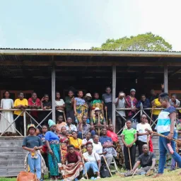 a group of people outdoors gathered in front of and on the porch of a building