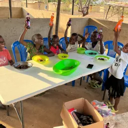 children seated at a table and holding up soda bottles