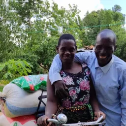 Members receiving welcome deliveries of maize and farm inputs. a man with his arm around a woman on a bicycle loaded with sacks of maize