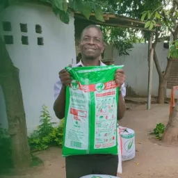 A member receives maize and farm inputs. a man holding up a sack of fertilizer