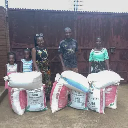 A family in Malawi who received farming inputs. a family standing behind bags of maize and farming inputs