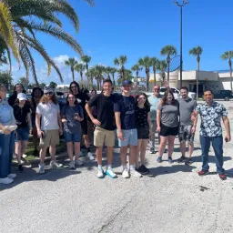 teens and young adults standing outside by a palm tree