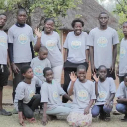 a group of children standing and sitting outside and waving
