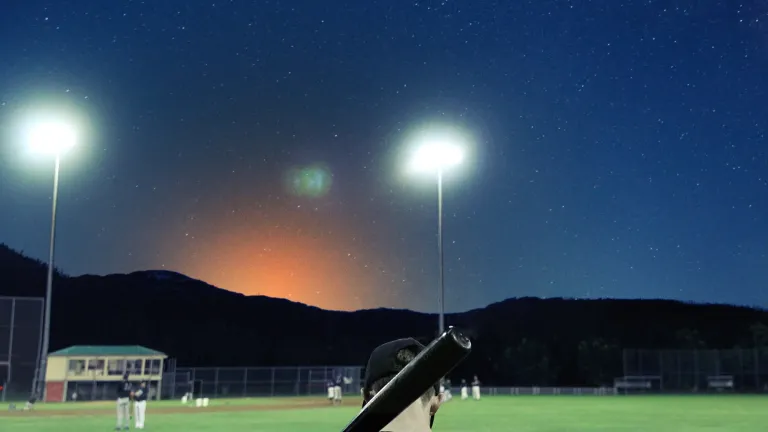 Young man holding a baseball bat on an empty ballfield at dusk