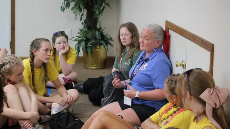 a woman talking to a group of girls seated in a circle