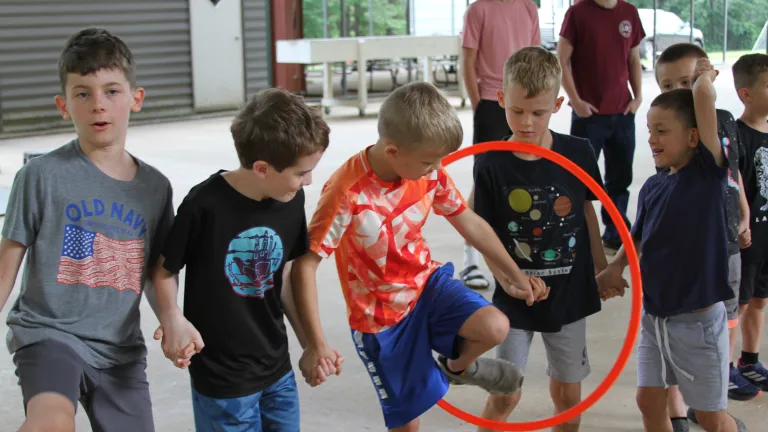 Kids holding hands walking through a hula hoop