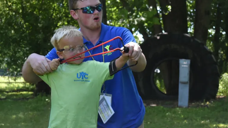 Staff member helping camper use a slingshot