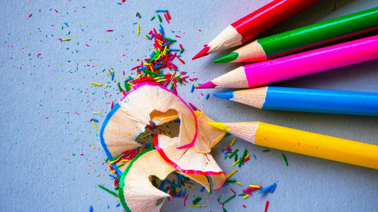 five differently colored pencils with a pile of pencil shavings