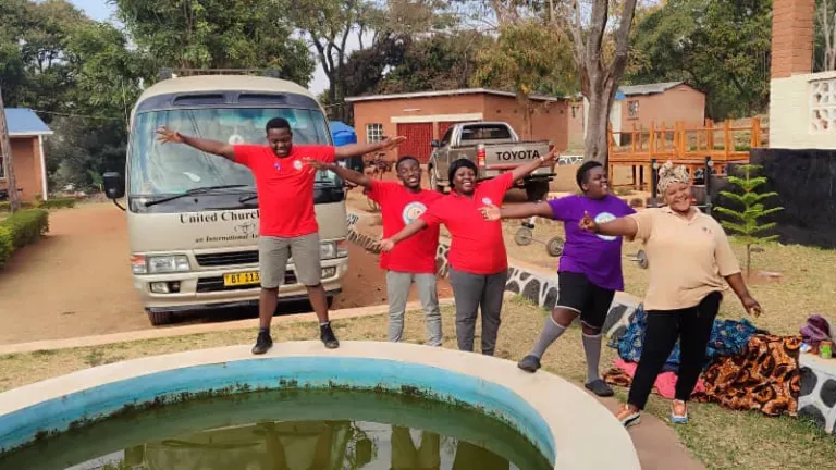 a group of children standing by a pool with the church bus parked behind them