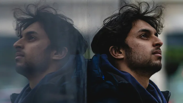 A man leaning against a shiny wall showing his reflection.