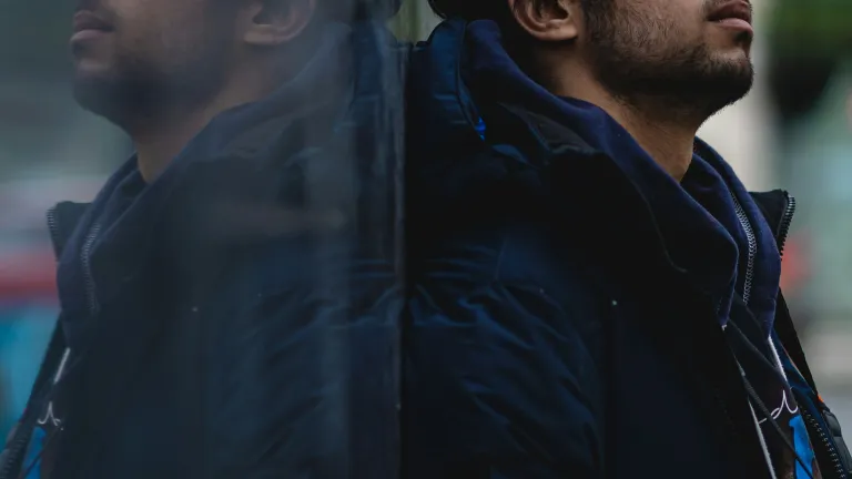A man leaning against a shiny wall showing his reflection.