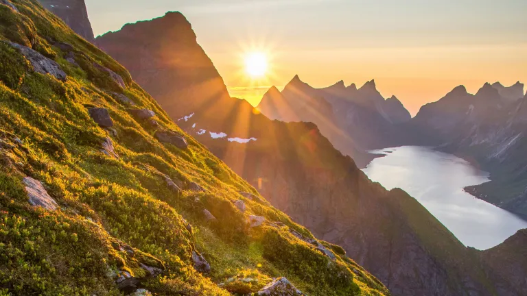 a mountainside with the sunset peeking through the horizon
