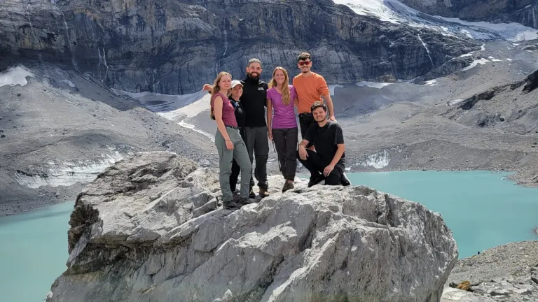 people standing on a large rock with mountains and a body of water in the background