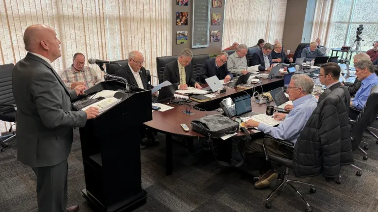 a group of men seated around a table and listening to a presenter at a lectern