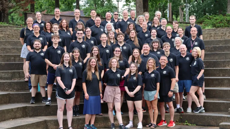 This year’s camp theme, “Building on the Foundation,” offered insights into understanding Jesus Christ as the cornerstone of the Church. a group of people in matching dark-colored shirts standing on a set of concrete steps