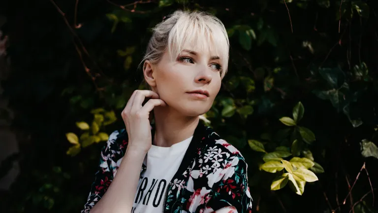 a woman with a reflective expression on her face and greenery behind her