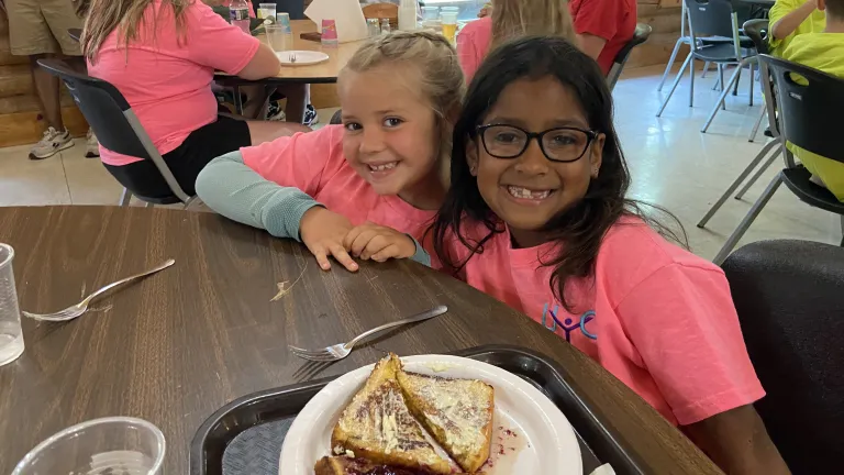 two girls sitting at a table with a sandwich