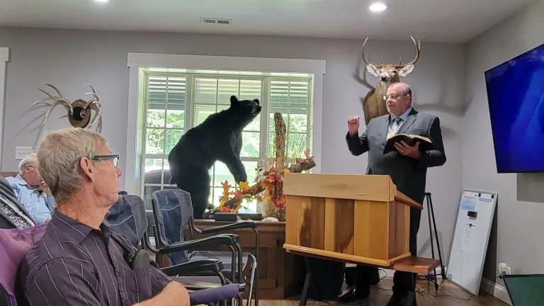 men seated indoors and listening to a man speaking at a lectern