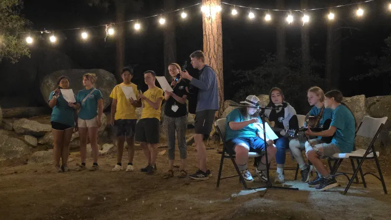 a group of teens singing with string lights overhead and musical instruments