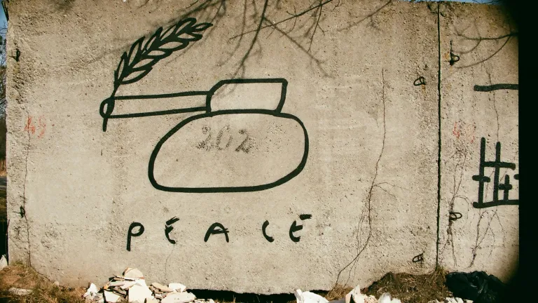 "Peace through strength" is a phrase that suggests that military power can help preserve peace, and it has been used by many American presidents. Hand-drawn tank on cement wall with peace written underneath.