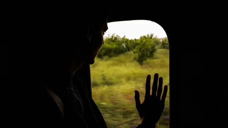 Silhouette of a man looking out train window with hand on the window