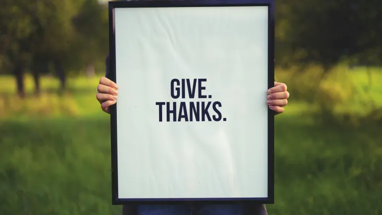 A person holding a sign that says: Give. Thanks.