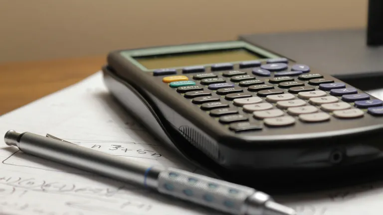 a calculator and pen sitting atop a notebook with calculations written in it