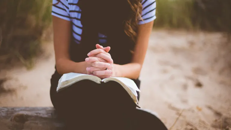 a woman sitting with folded hands on an open Bible