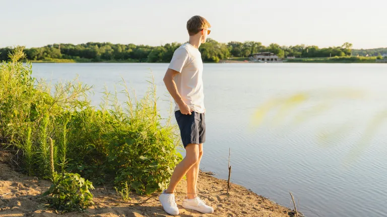 A teenage boy walking by a lake.