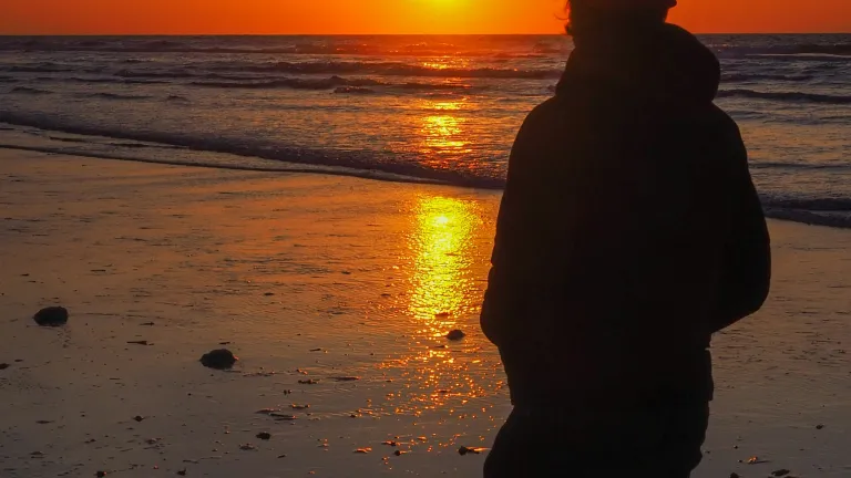 A young man walking on the beach while the sun is setting.